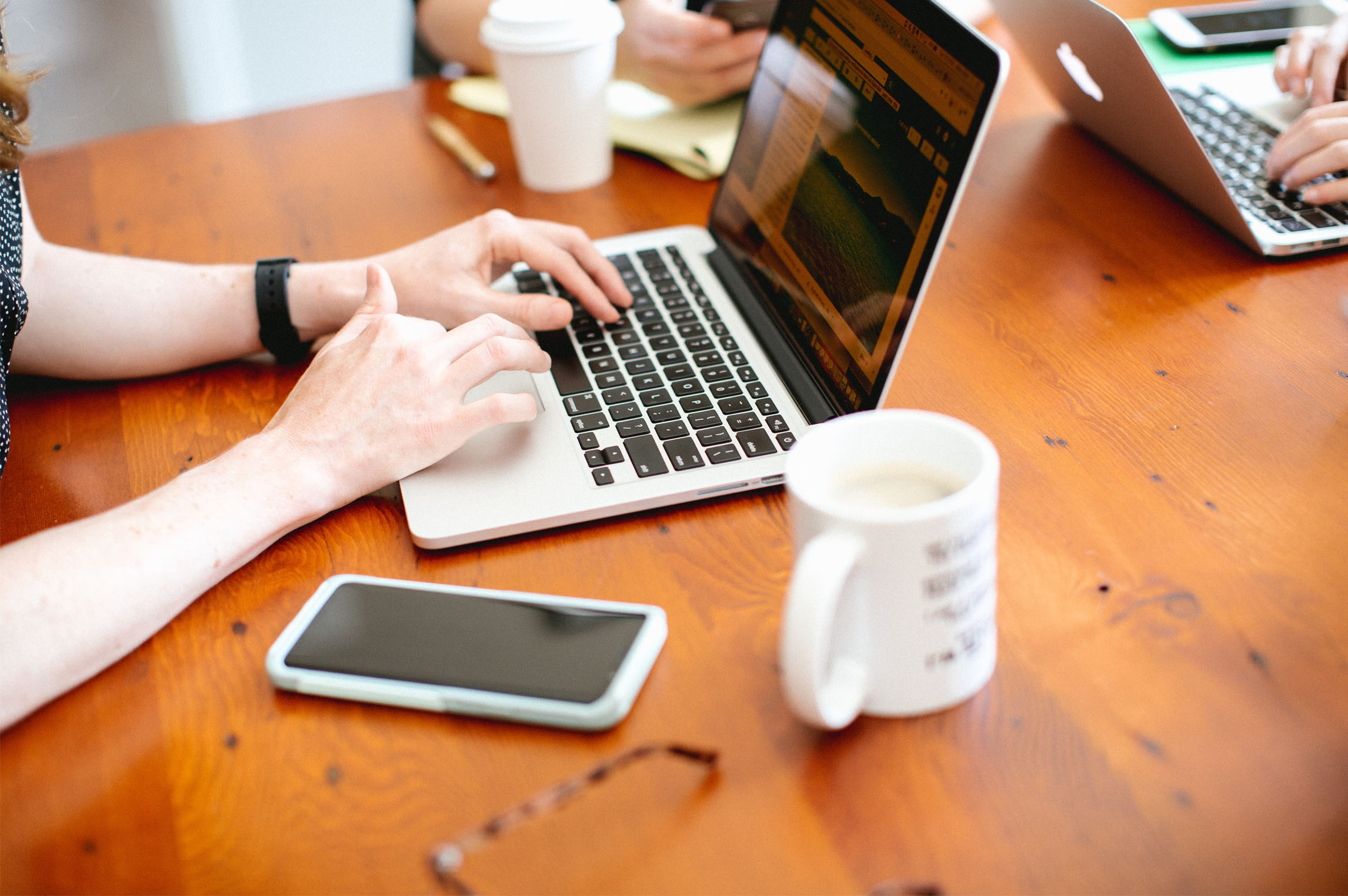 Woman using laptop with coffee mug and cellphone